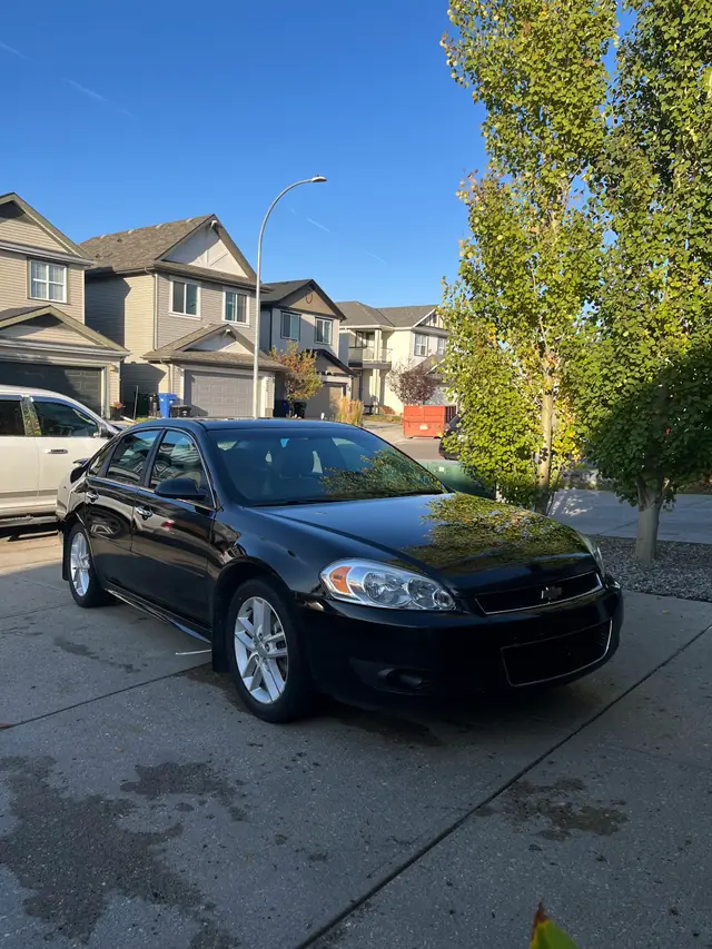 A black Chevrolet Impala parked in a neighbourhood driveway after a detail, clean paint under a blue sky