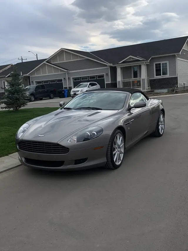 Grey Aston Martin DB9 Volante at a residential curb, paint holding a clean reflection of the sky